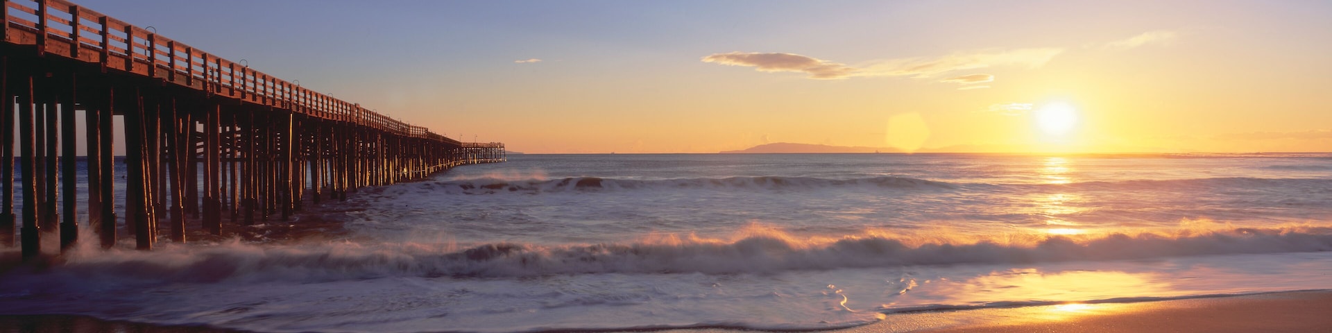 A wooden pier extending into the ocean at sunset.