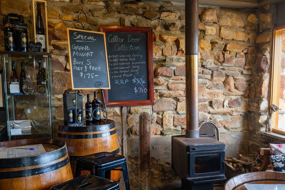 A rustic cellar with wooden barrels, a stone wall, and a wood-burning stove.
