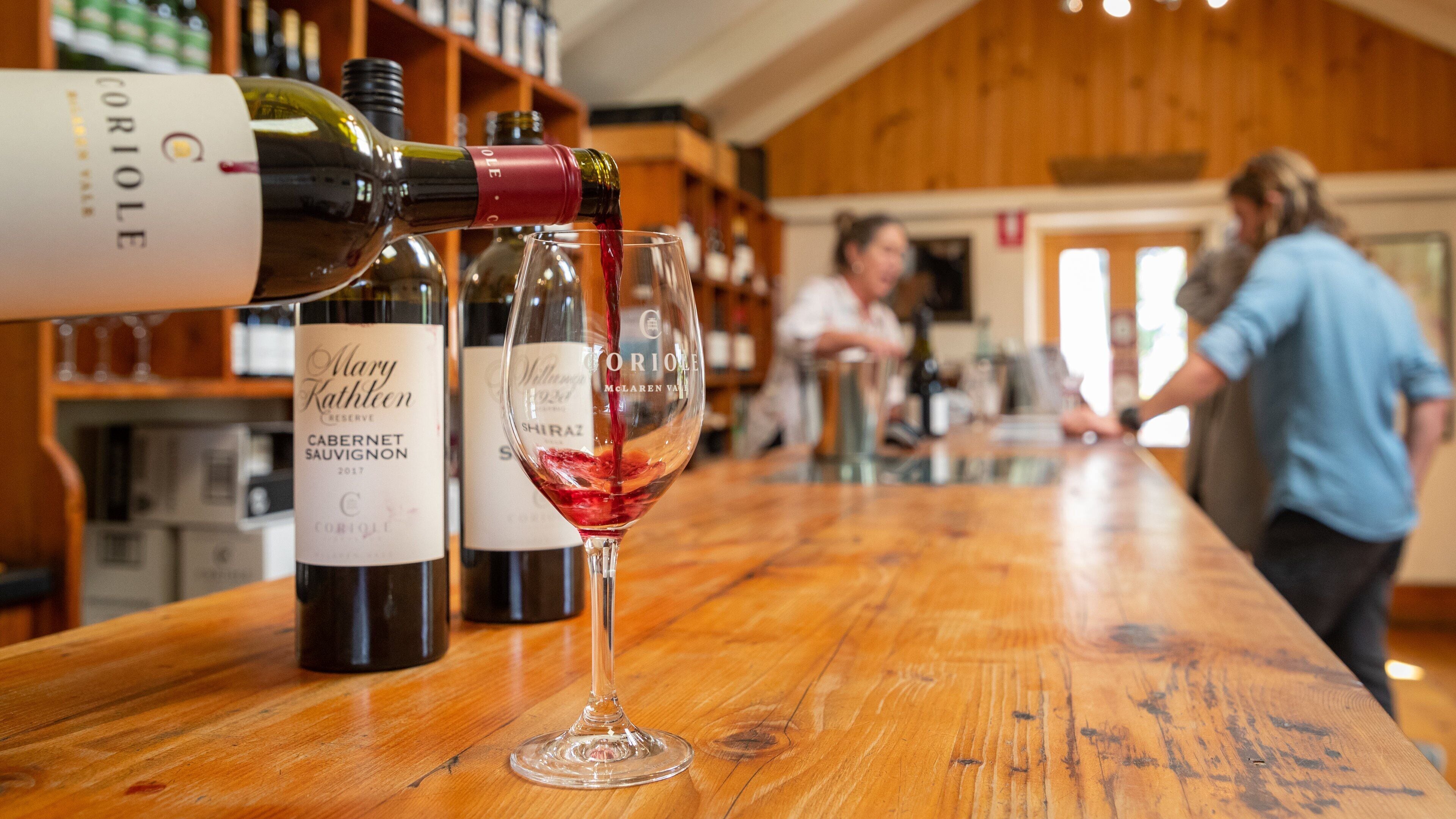 A wine bottle being poured into a glass at a bar with wooden shelves and a rustic interior.