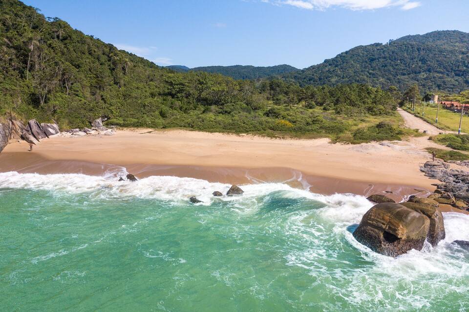 A beach with clear turquoise water, a sandy shore, and a forested hillside in the background.