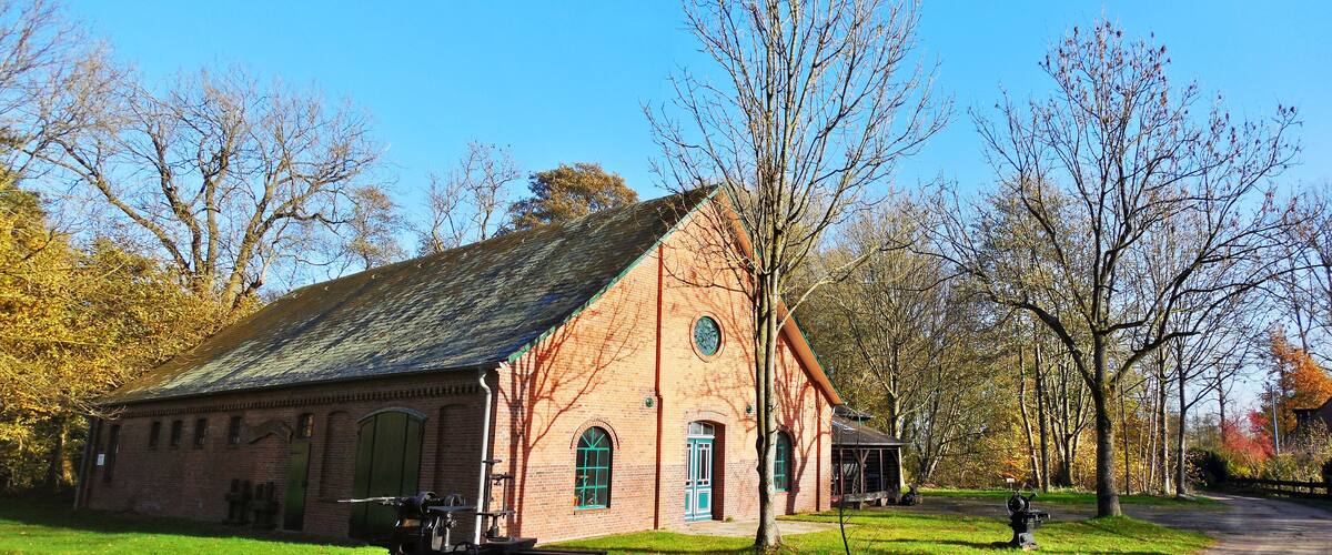 A historic brick building with a green door and windows, surrounded by trees and a grassy area.