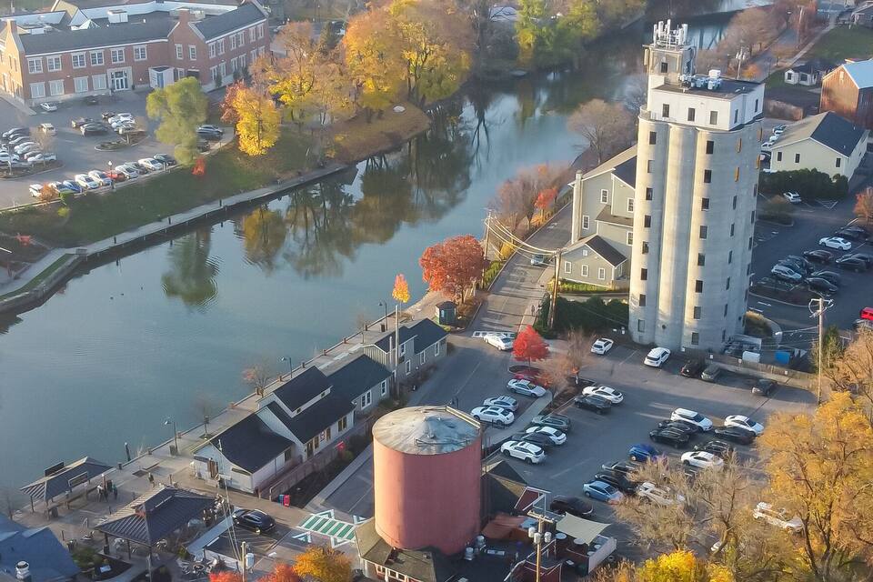 An aerial view of a town with a river, parking lots, and autumn-colored trees.