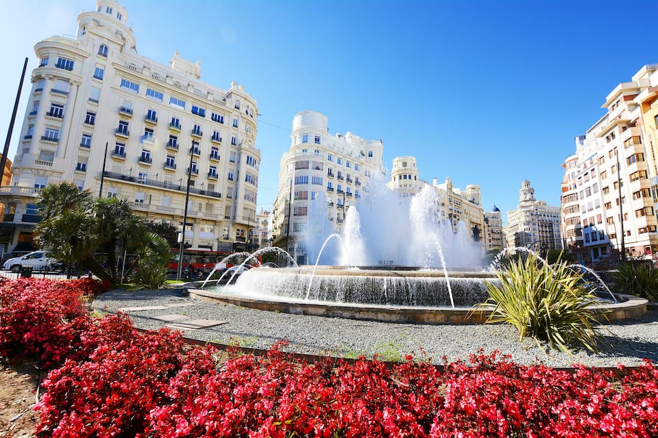 Une fontaine entourée de fleurs rouges et de bâtiments modernes.