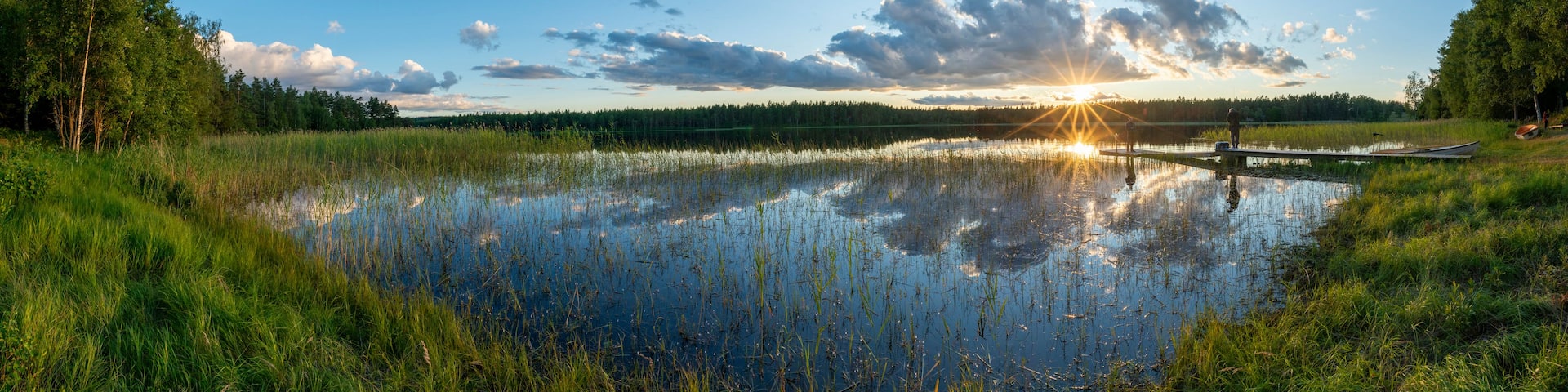 A serene lake with a wooden dock, surrounded by lush greenery and a clear sky.