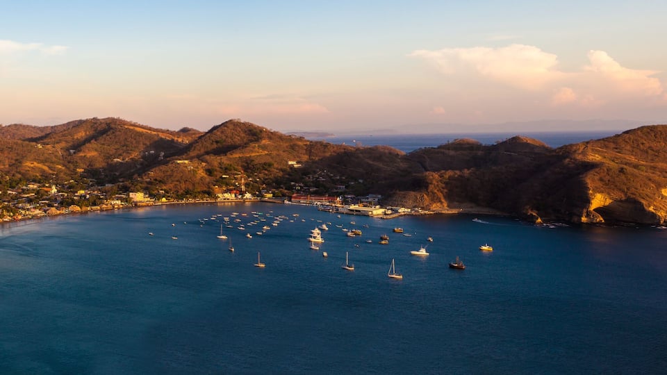 Un pueblo costero con una bahía llena de barcos, rodeado de colinas.