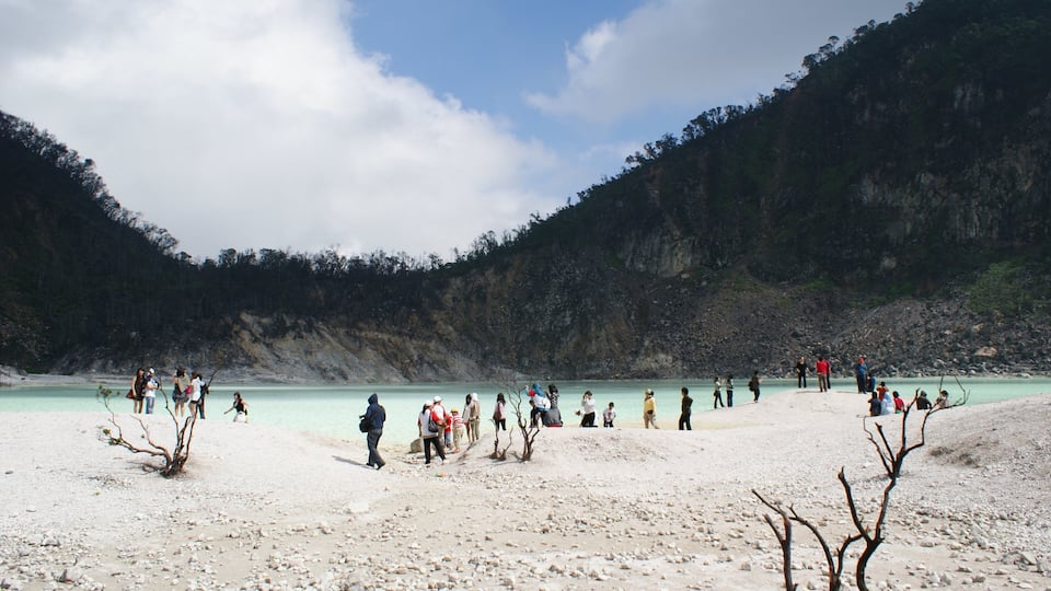 A group of people at a beach with clear turquoise water and rocky cliffs in the background.