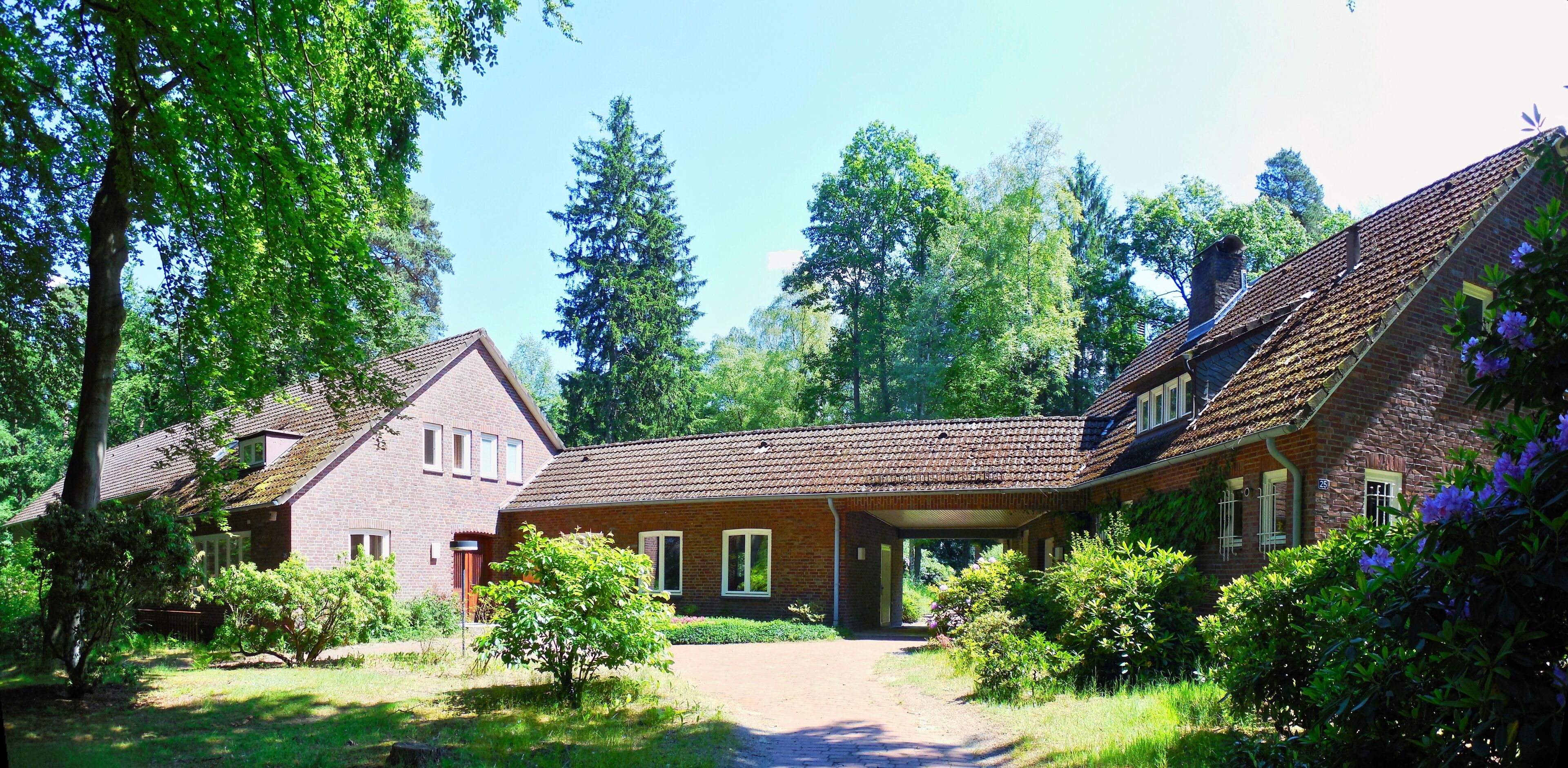 A brick house with a sloped roof, surrounded by lush greenery and trees.