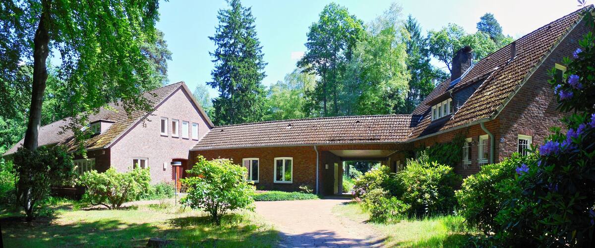 A brick house with a sloped roof, surrounded by lush greenery and trees.