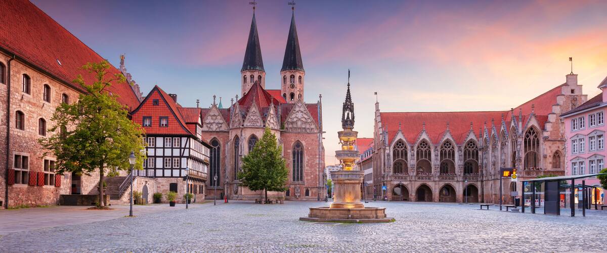 A historic square with a prominent church featuring twin spires, a fountain, and traditional half-timbered buildings.