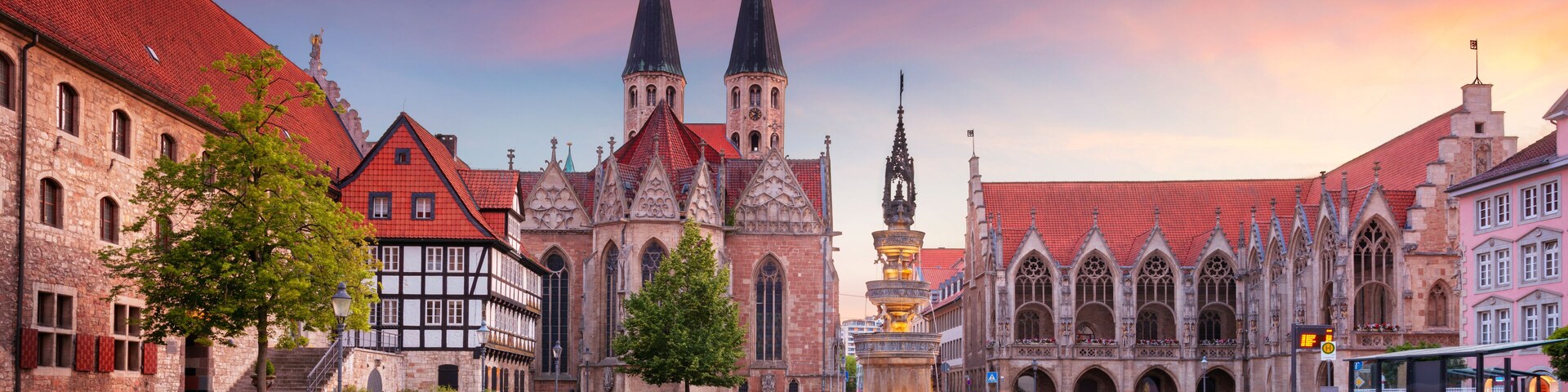 A historic square with a prominent church featuring twin spires, a fountain, and traditional half-timbered buildings.
