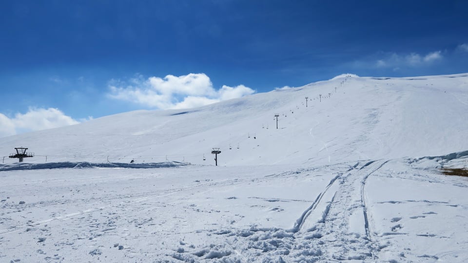 A snow-covered ski slope with ski lifts and tracks.