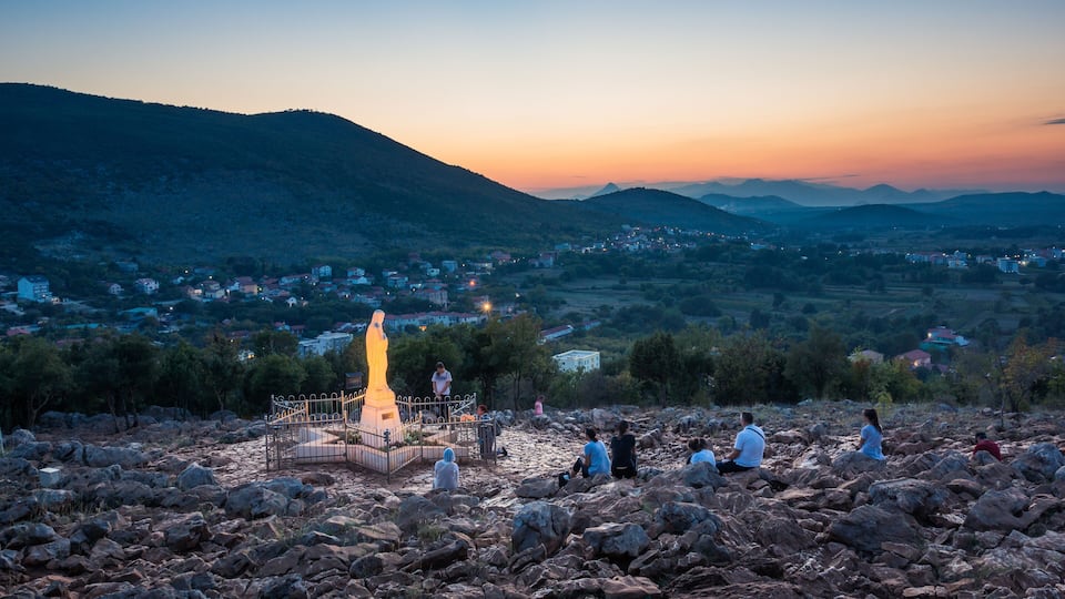 A rocky landscape with a statue and people sitting around it.