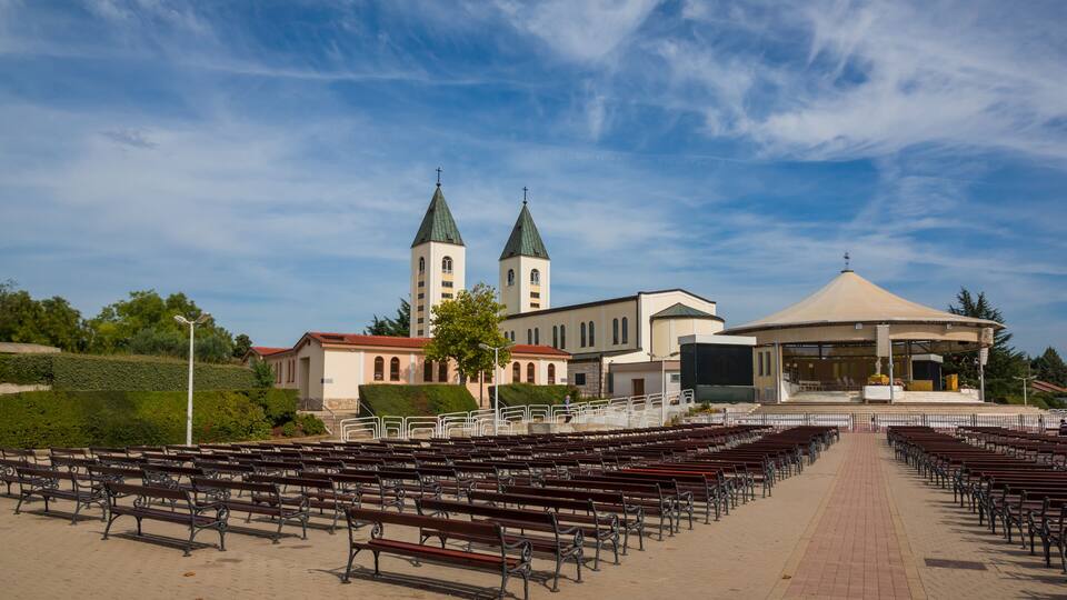 A church with two towers and a central dome, surrounded by rows of benches.