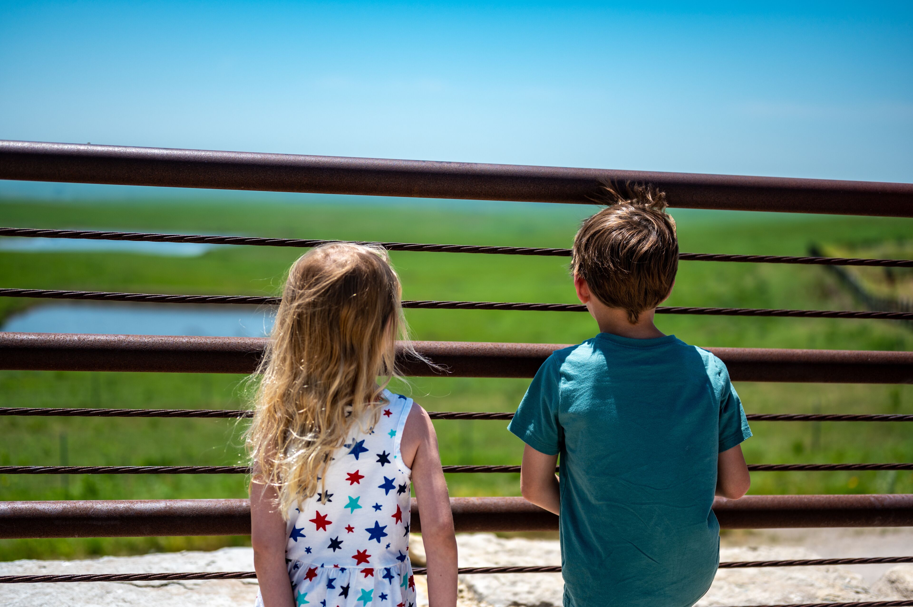 Children looking through a fence at the Feed Yard Scenic Overlook outside of Dodge City, Kansas.