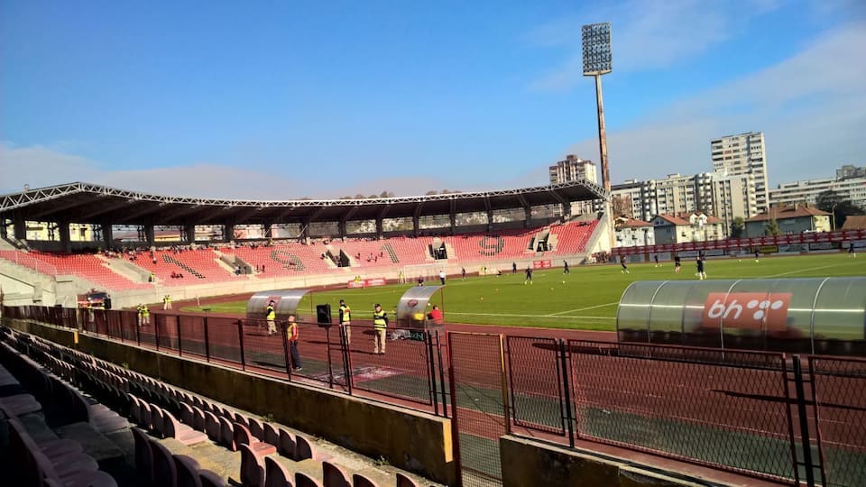 A stadium with red seats, a football field, and a tall floodlight tower.