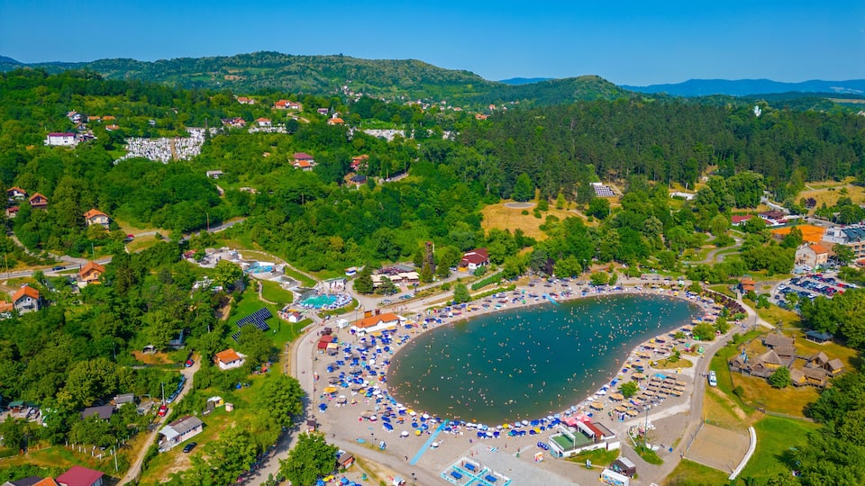 An aerial view of a coastal town with a large beach, houses, and surrounding hills.