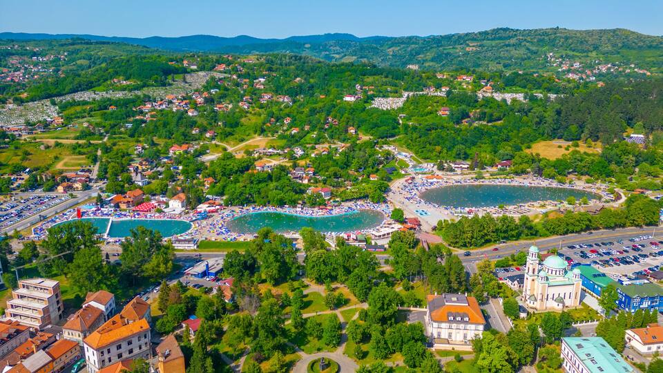An aerial view of a coastal town with a large beach, swimming pools, and a historic church.