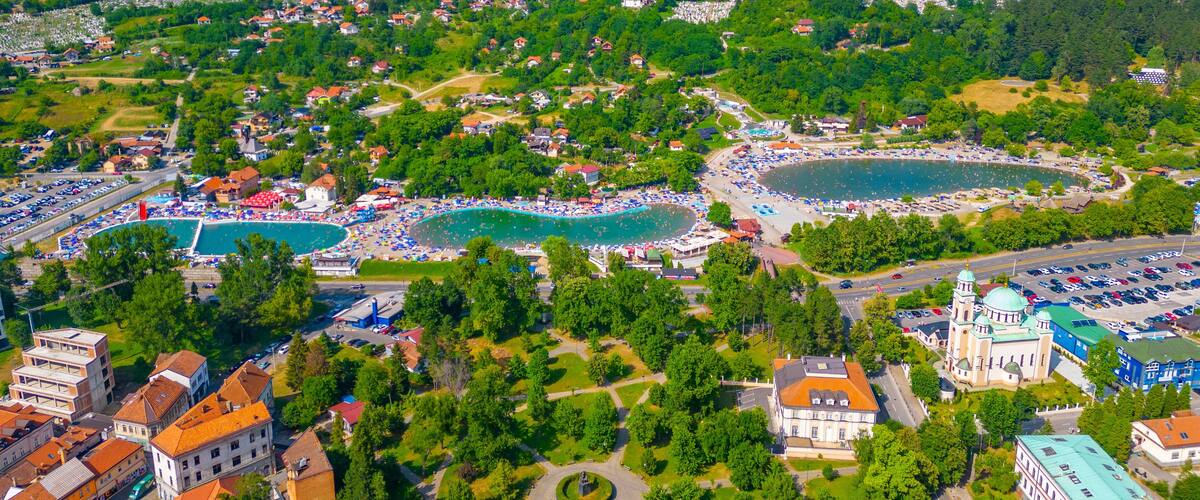 An aerial view of a coastal town with a large beach, swimming pools, and a historic church.