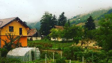 Paisaje rural con una casa amarilla, un invernadero y un huerto.