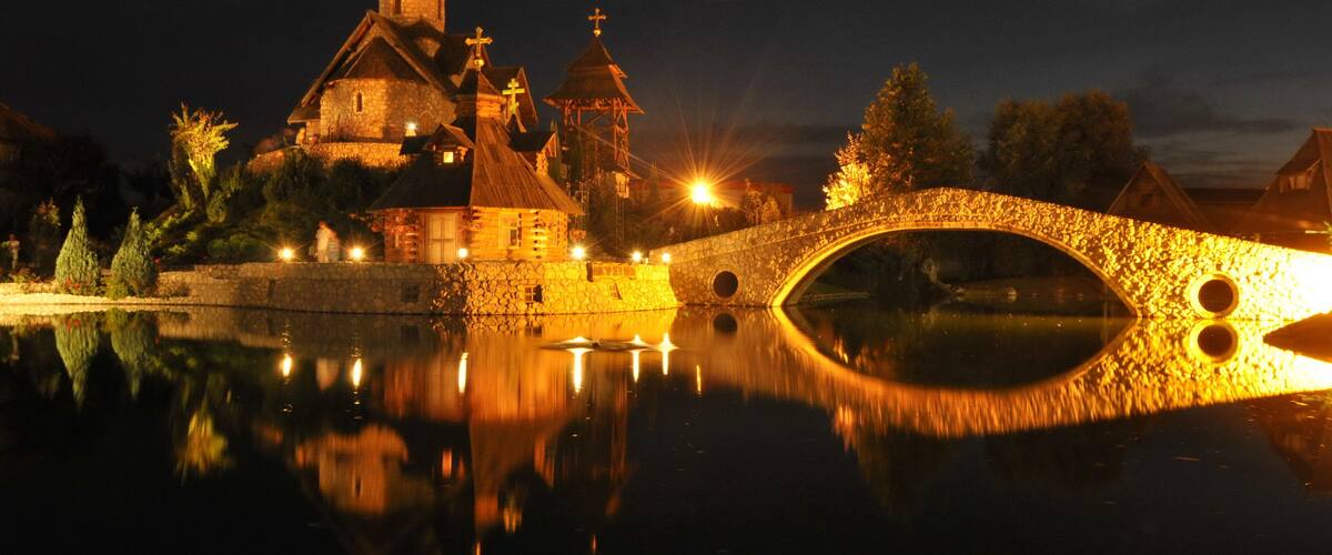A stone bridge over a calm river reflecting a historic church with multiple spires and a tower.