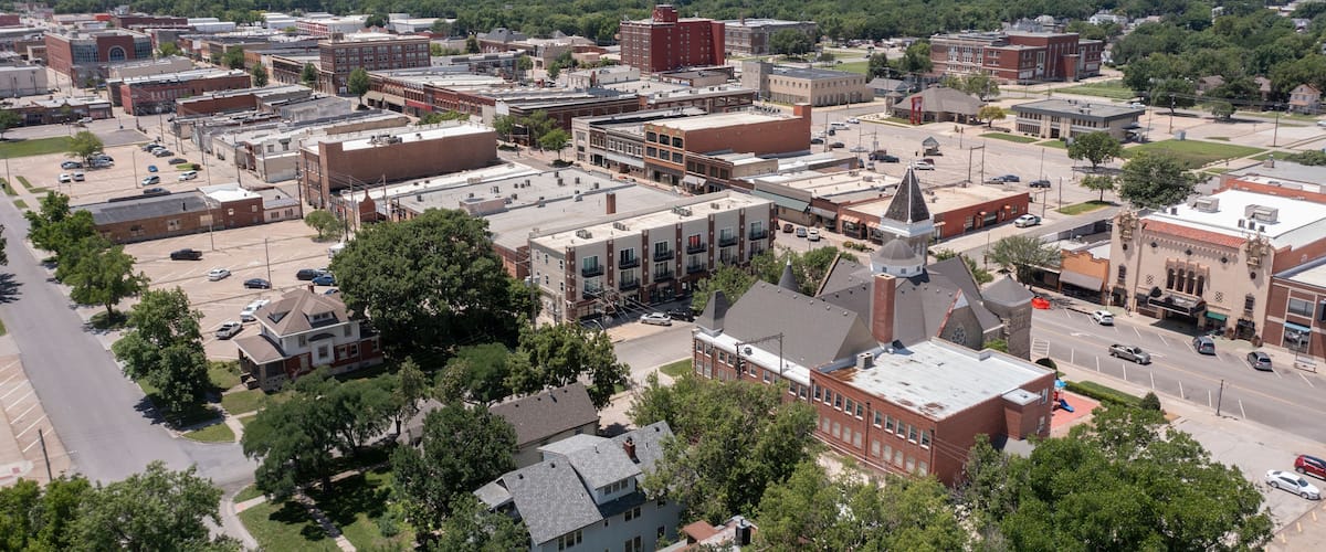 A town with a mix of historic and modern buildings, a prominent church with a steeple, and a large industrial area in the distance.