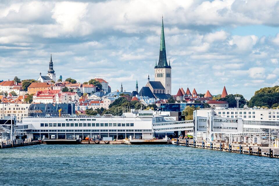 Ein Hafen mit einem großen weißen Gebäude, einem hohen Kirchturm und mehreren Gebäuden mit roten Dächern.