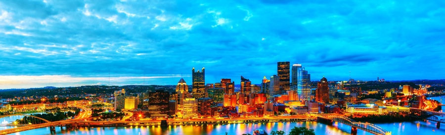 A city skyline with illuminated buildings, a river, and a bridge.
