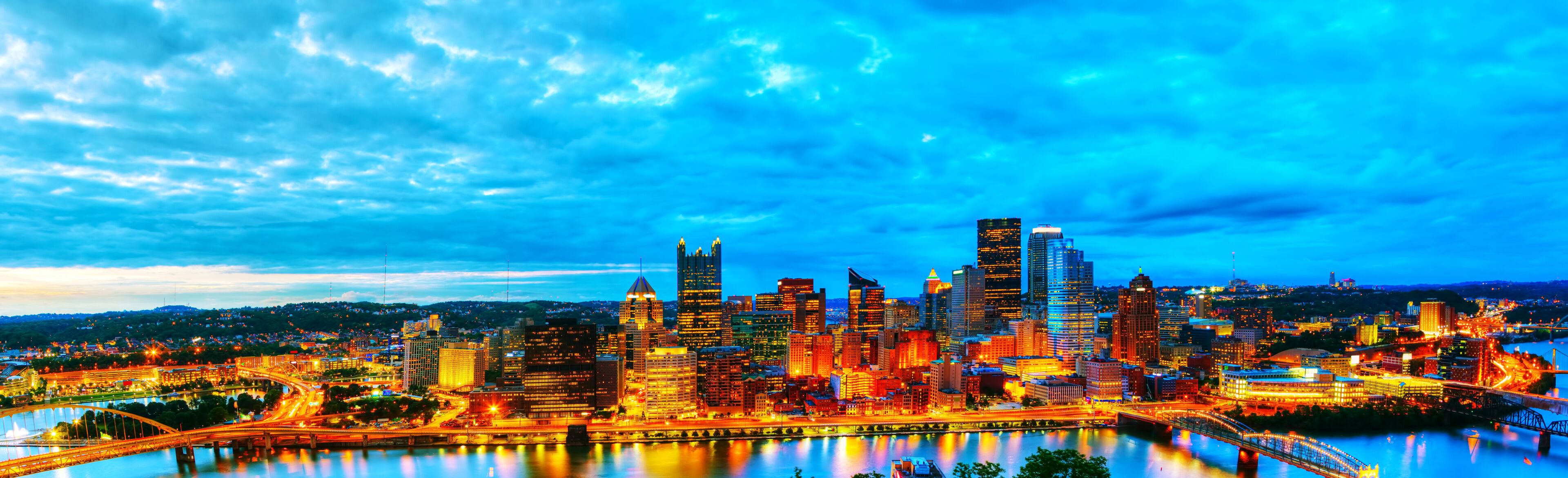 A city skyline with illuminated buildings, a river, and a bridge.