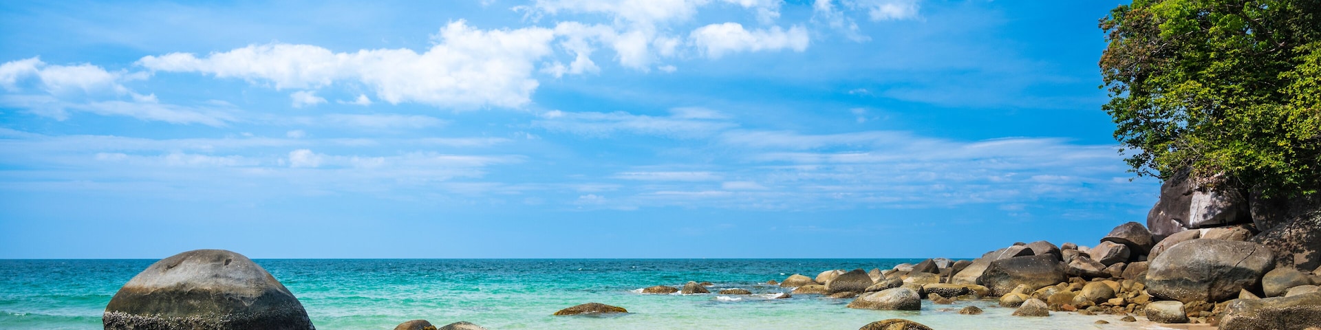 A beach with clear turquoise water, large rocks, and a clear blue sky.