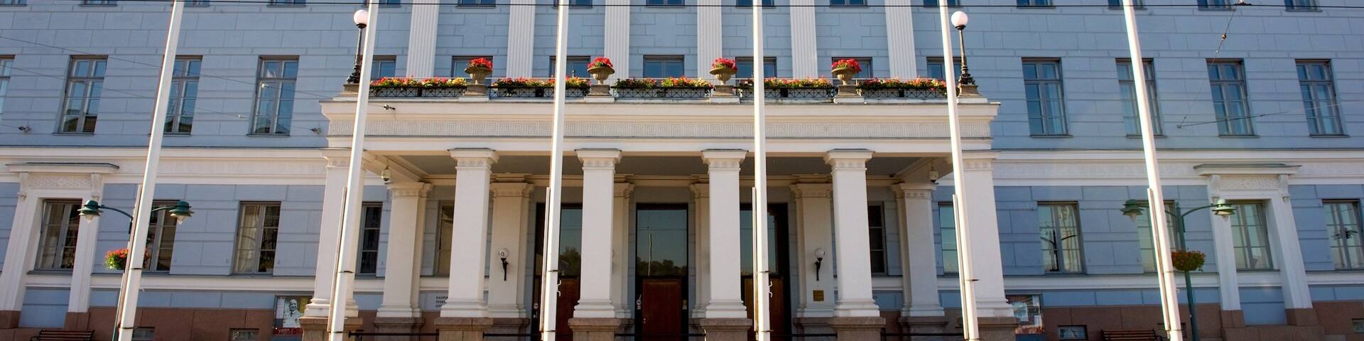 A large neoclassical building with a central entrance flanked by columns, a triangular pediment, and a flagpole.