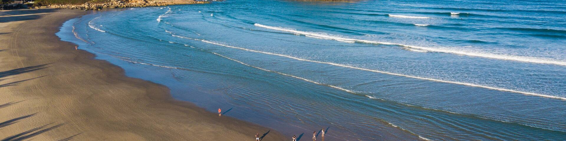 A beach with waves, a small island, and a clear sky.