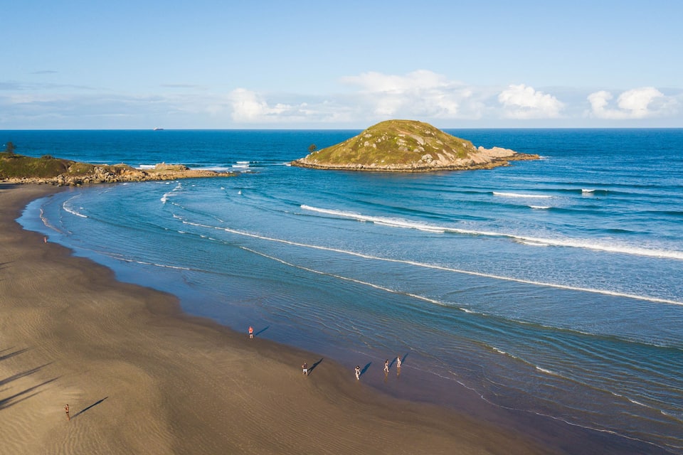 A beach with waves, a small island, and a clear sky.