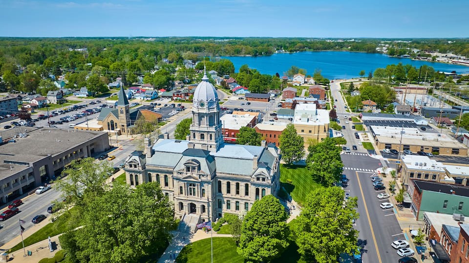 A town with a prominent historic building, a large body of water, and surrounding greenery.