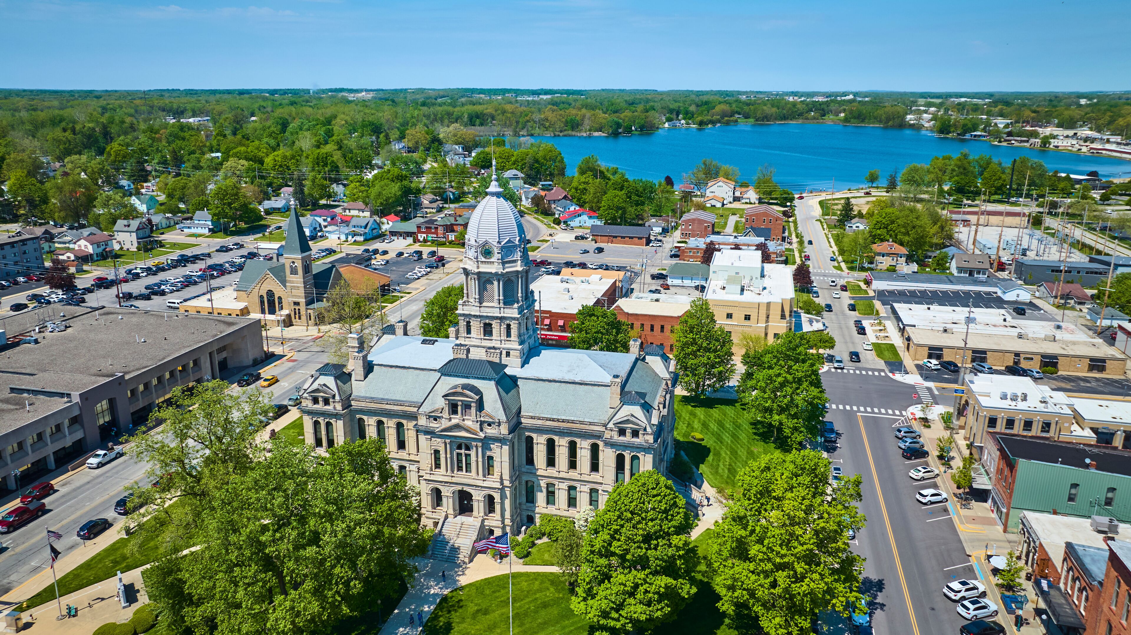 A town with a prominent historic building, a large body of water, and surrounding greenery.