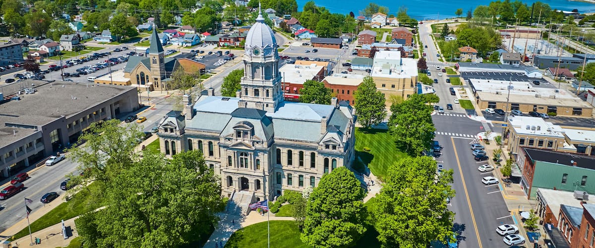 A town with a prominent historic building, a large body of water, and surrounding greenery.