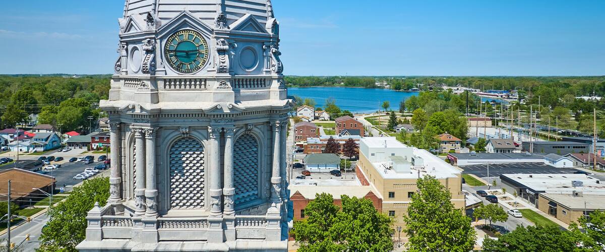 A clock tower with a dome and Roman numerals, overlooking a town with a lake in the background.
