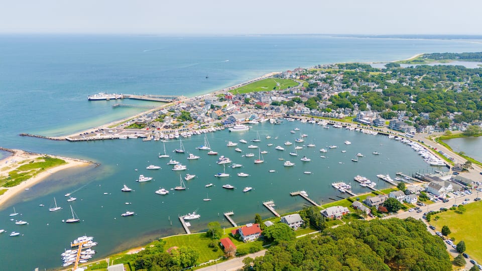 A coastal town with a marina filled with boats, surrounded by greenery and residential areas.