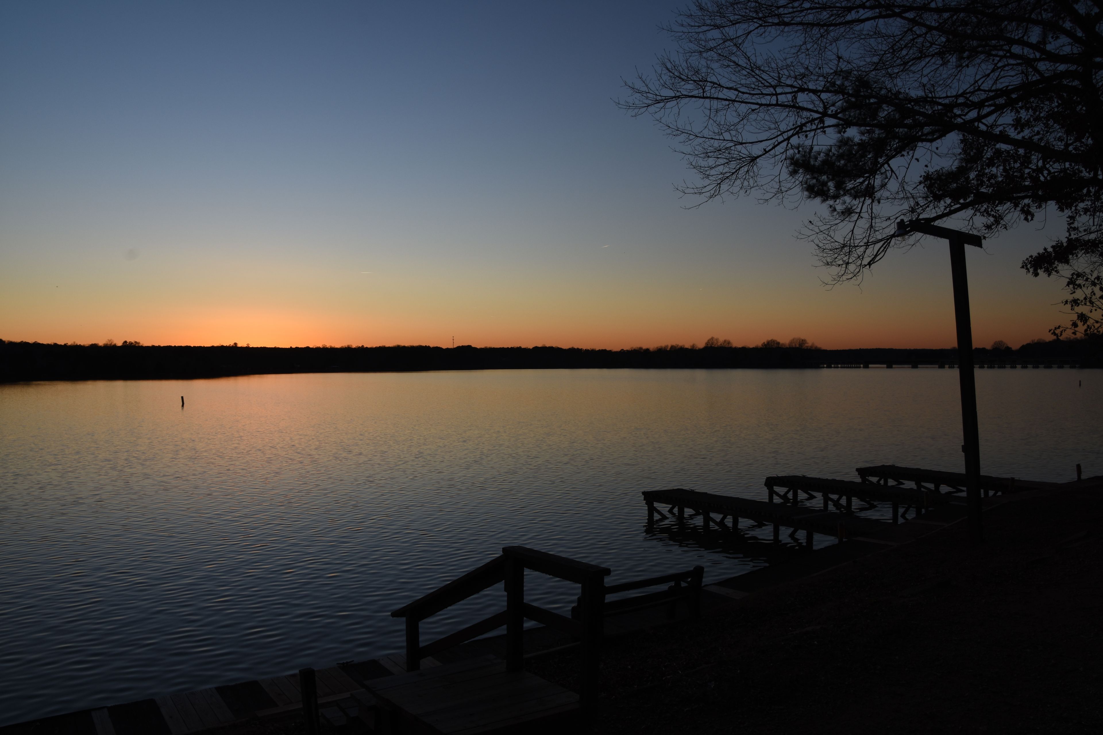 A sunset over a calm lake with a dock and trees in the foreground.