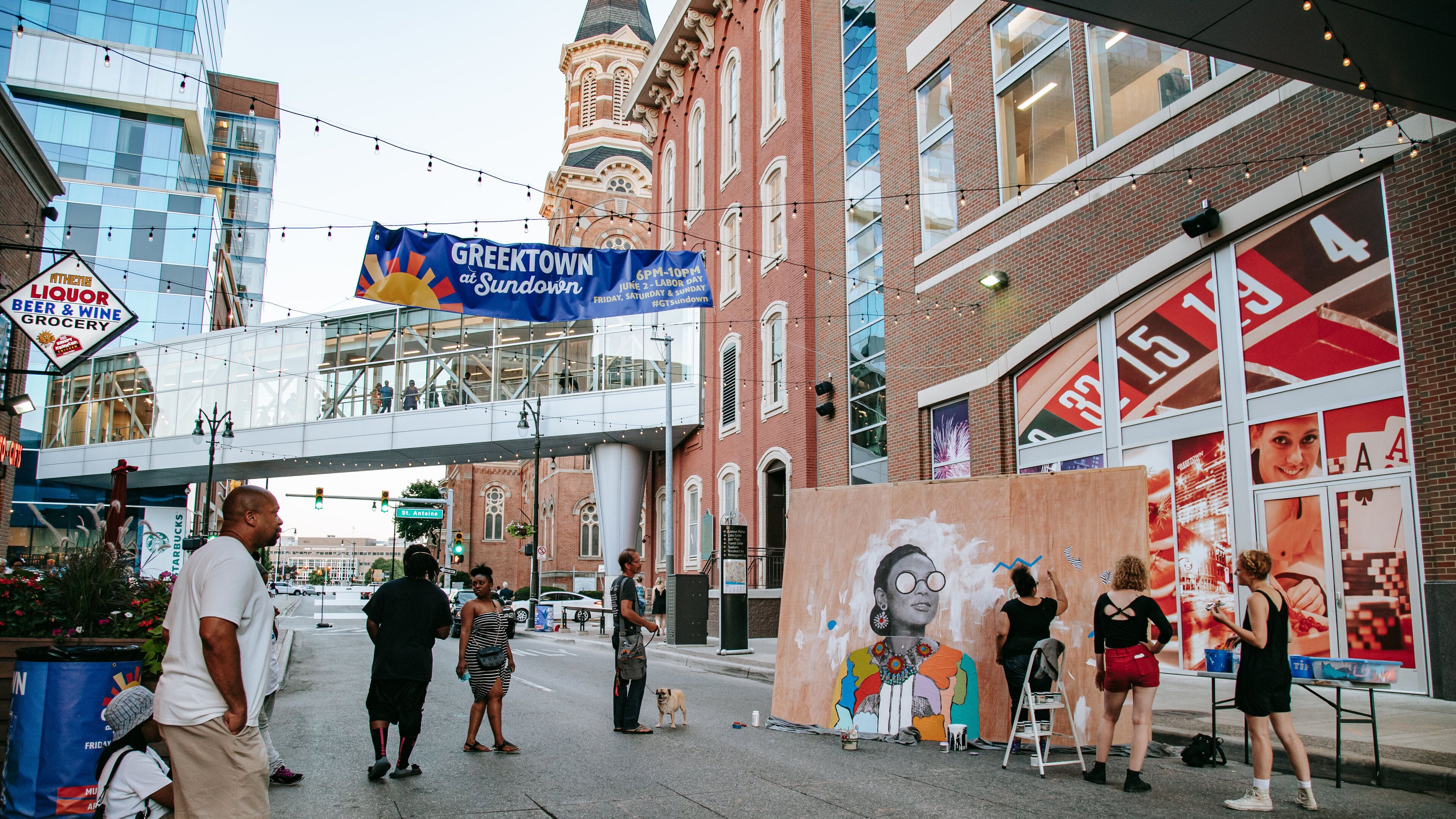 A street with a Greek Town banner, a Starbucks, and a mural on a building.