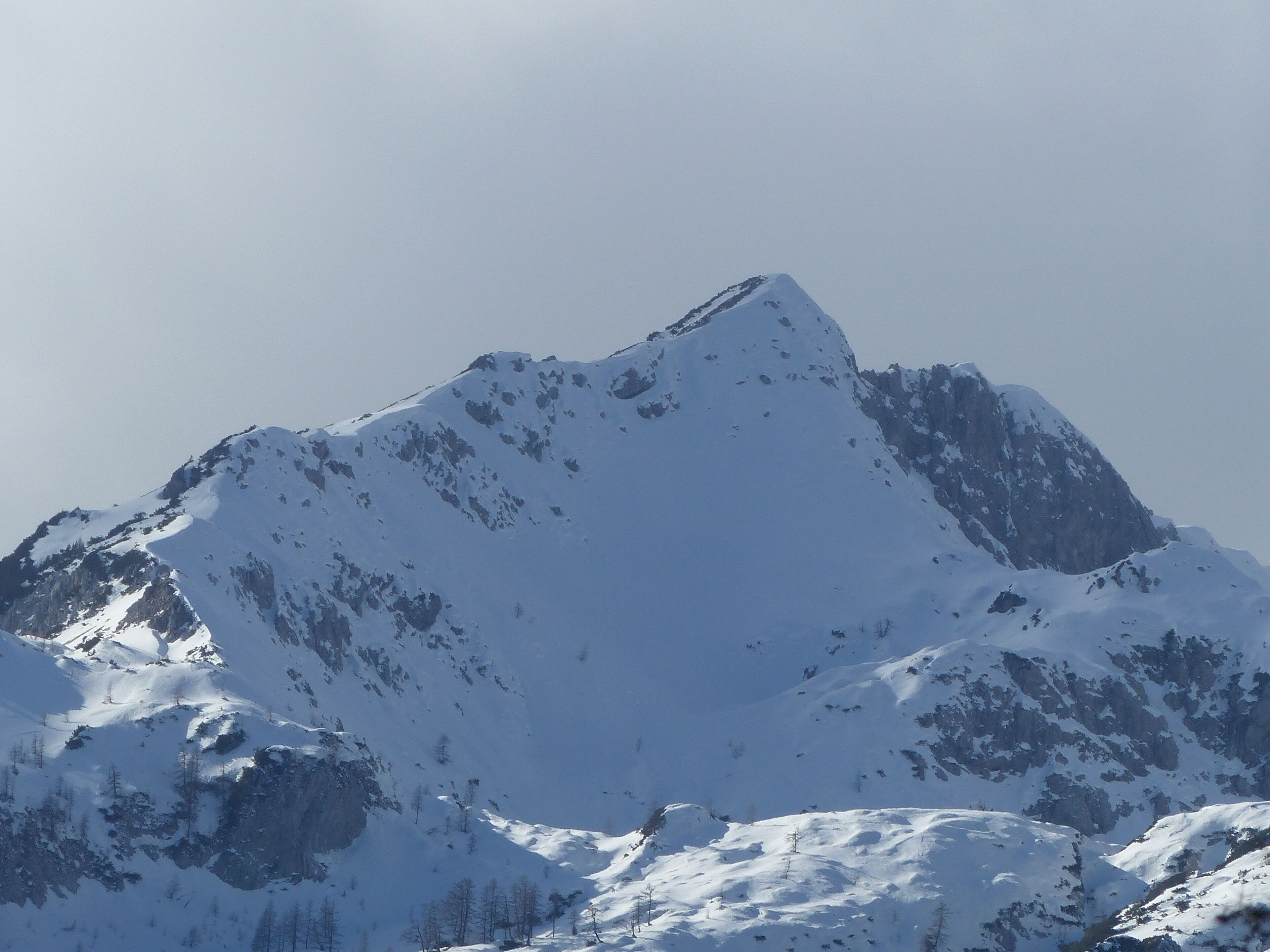 A snow-covered mountain peak with rugged terrain and sparse vegetation.