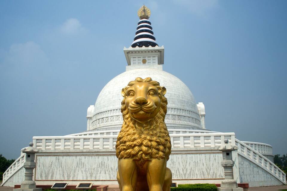 A large golden lion statue in front of a white temple with a striped spire.