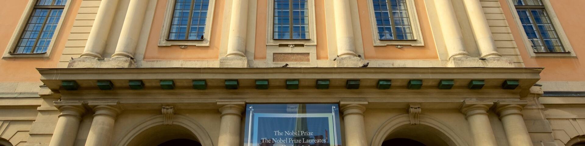 A neoclassical building with columns, a pediment, and a banner reading "The Nobel Prize Laureates Alfred Nobel".