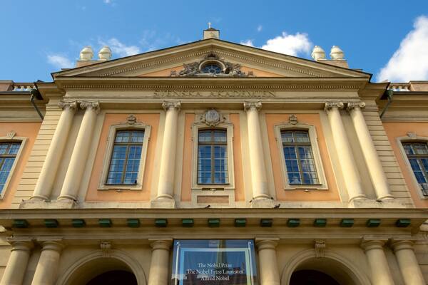 A neoclassical building with columns, a pediment, and a banner reading "The Nobel Prize Laureates Alfred Nobel".