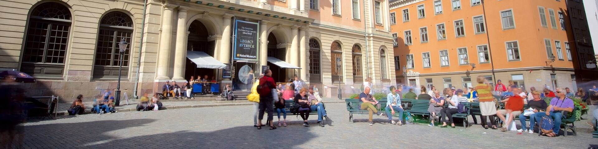 Un edificio histórico con arquitectura clásica, una torre de reloj y una multitud de personas en una plaza pública.
