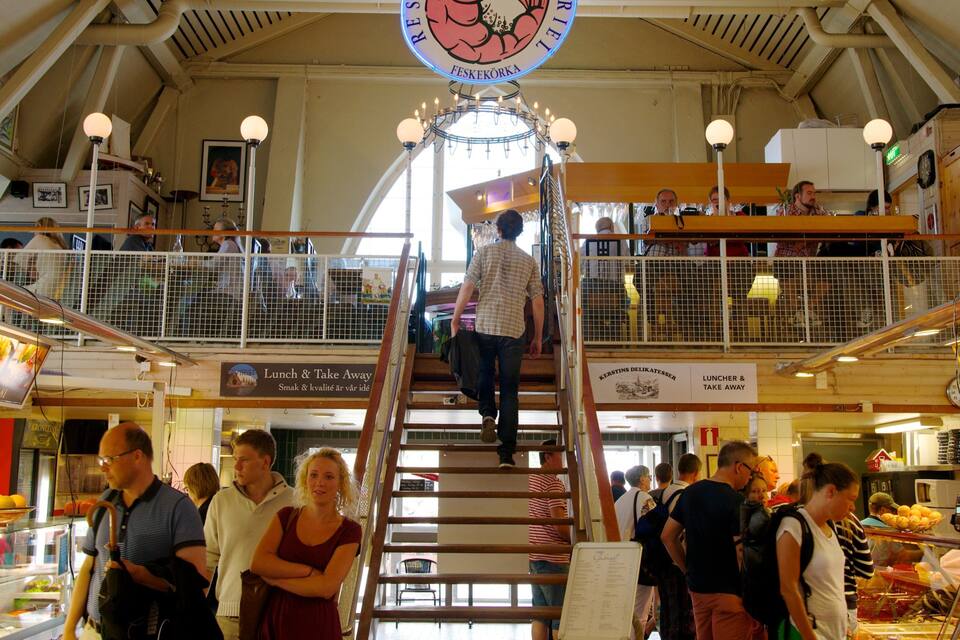 Un marché couvert animé, avec un escalier central, divers stands de nourriture et une enseigne indiquant « Déjeuner et plats à emporter ».