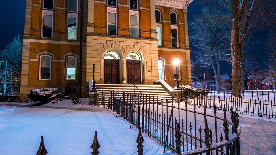 A historic building with a clock tower, surrounded by snow and a metal fence.
