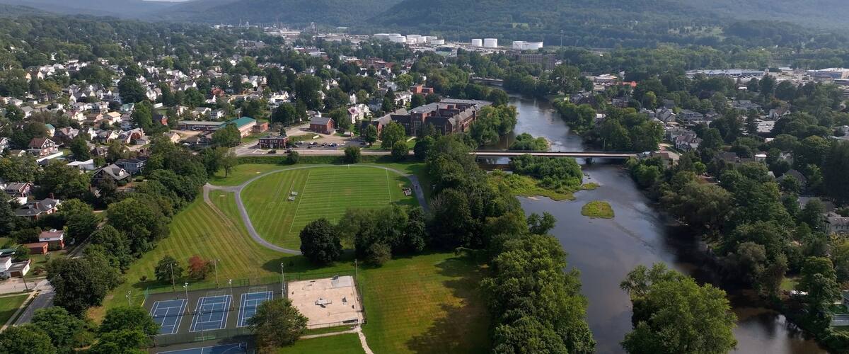 An aerial view of a town with a river, green fields, and a bridge.