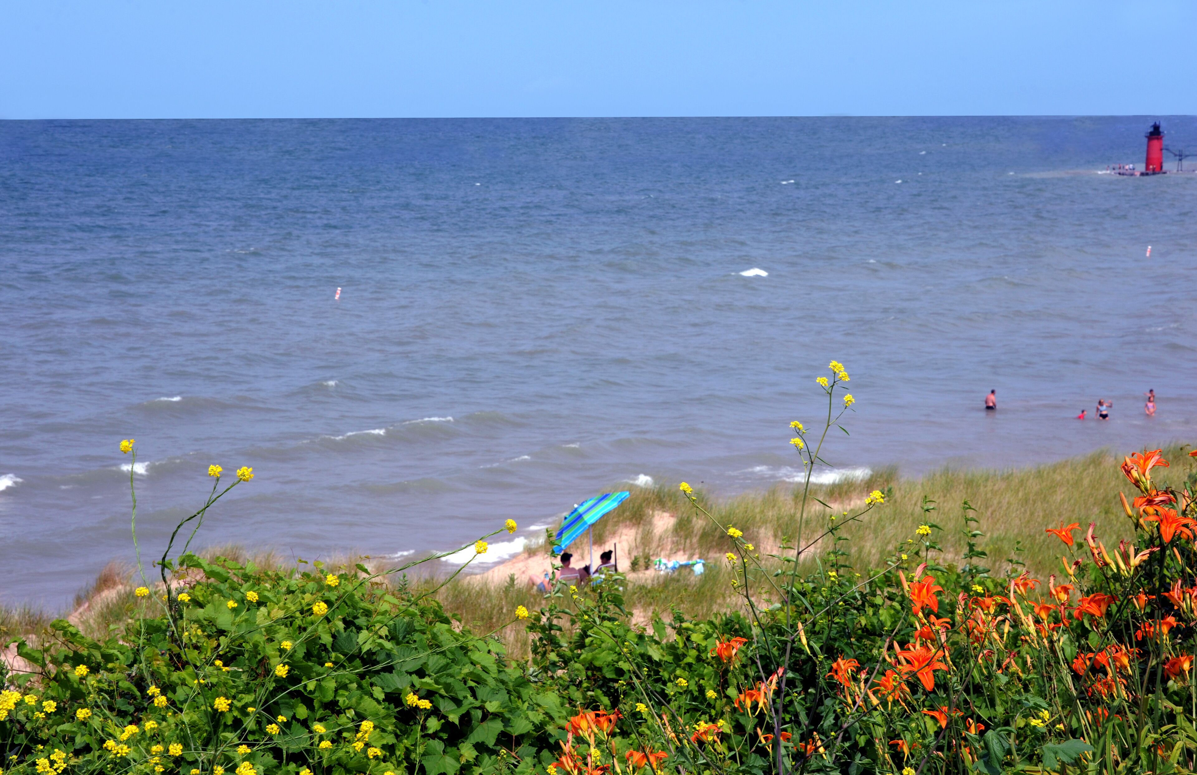 A beach with waves, a lighthouse, and people swimming.