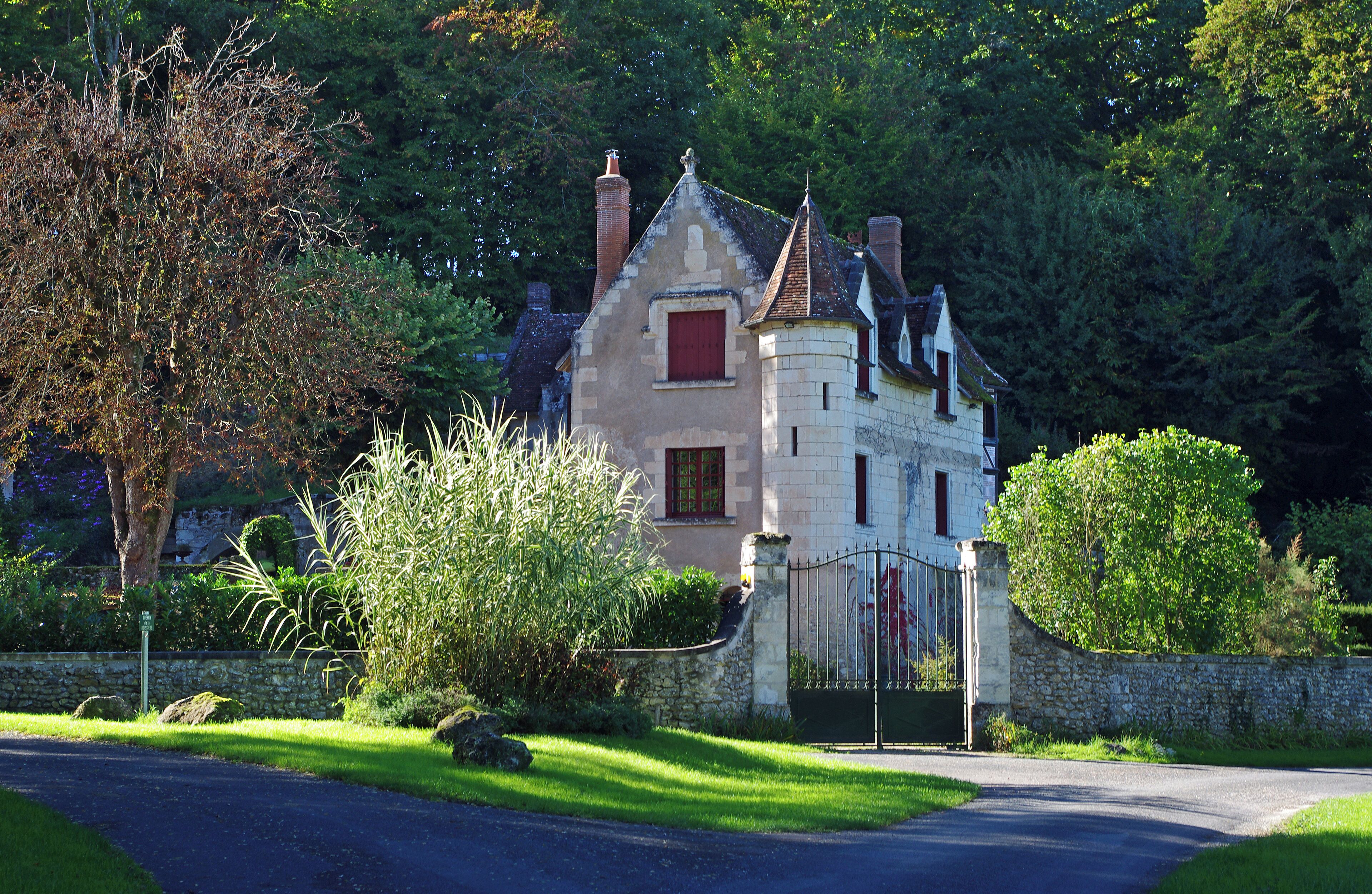A stone house with a red window and a black gate, surrounded by lush greenery and trees.