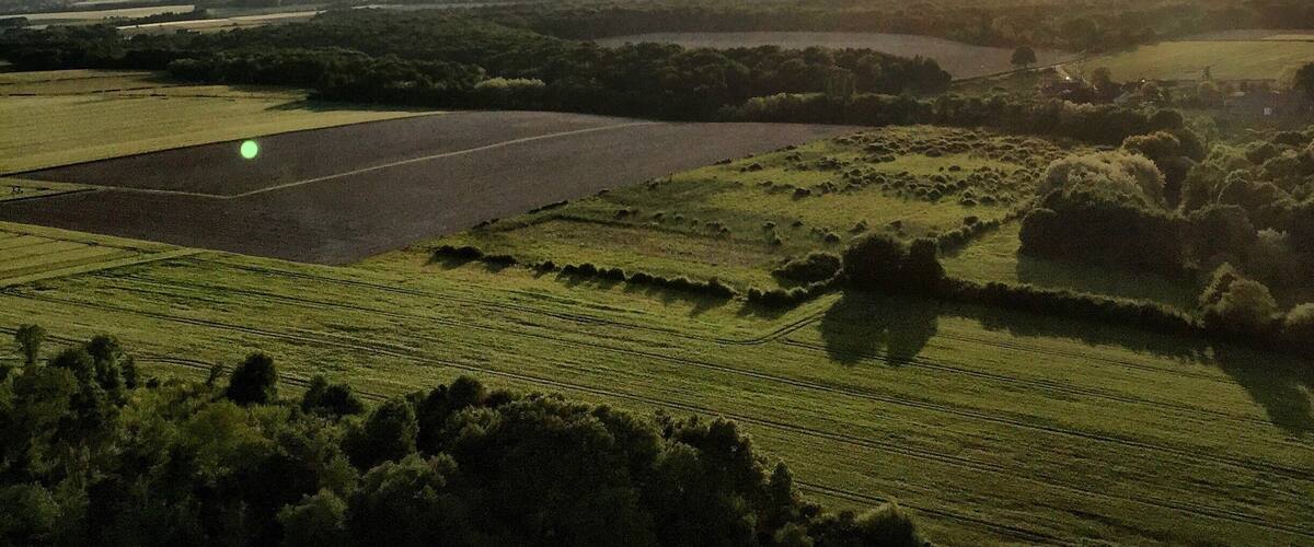 Two hot air balloons flying over a rural landscape with fields and a river.